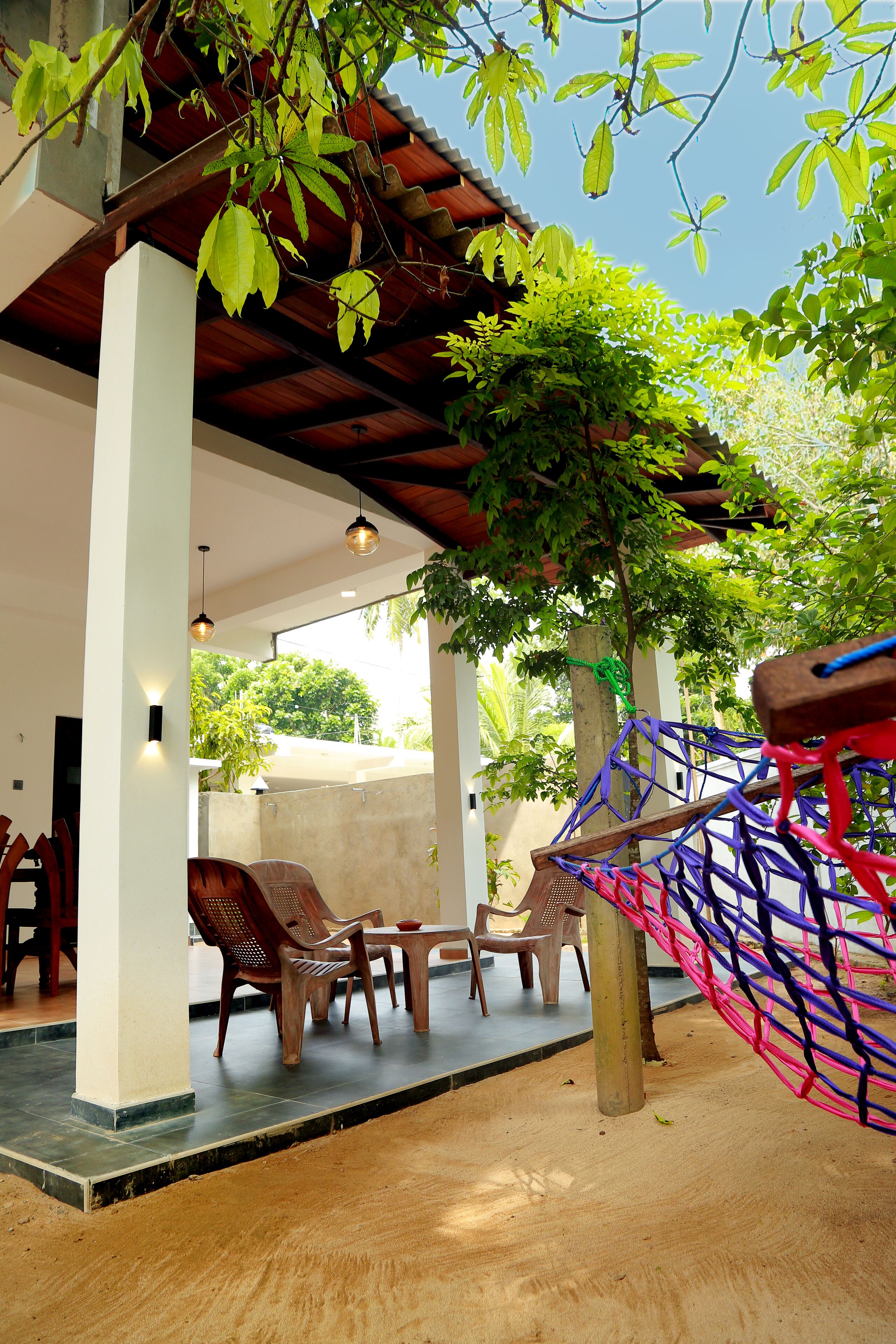 Un espace extérieur aménagé avec des chaises et un hamac, installé sous une pergola en bois et entouré de verdure.
