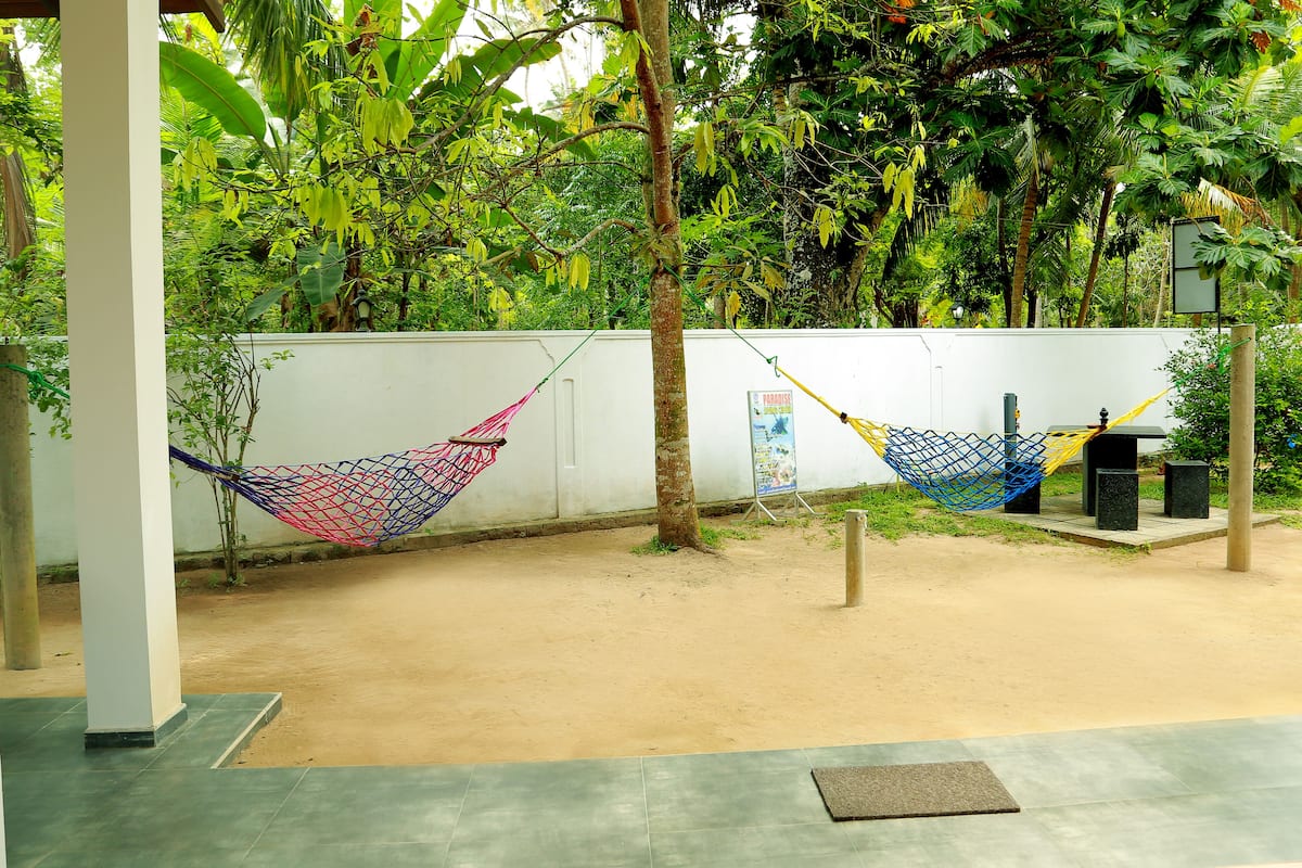 A hammock tied between two trees in a garden area with a white wall and a tiled floor.