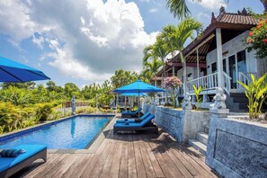 A pool area with lounge chairs and umbrellas, surrounded by tropical plants and a traditional building. - Tatak Bunut Villa Nusa Ceningan (Ceningan Island)