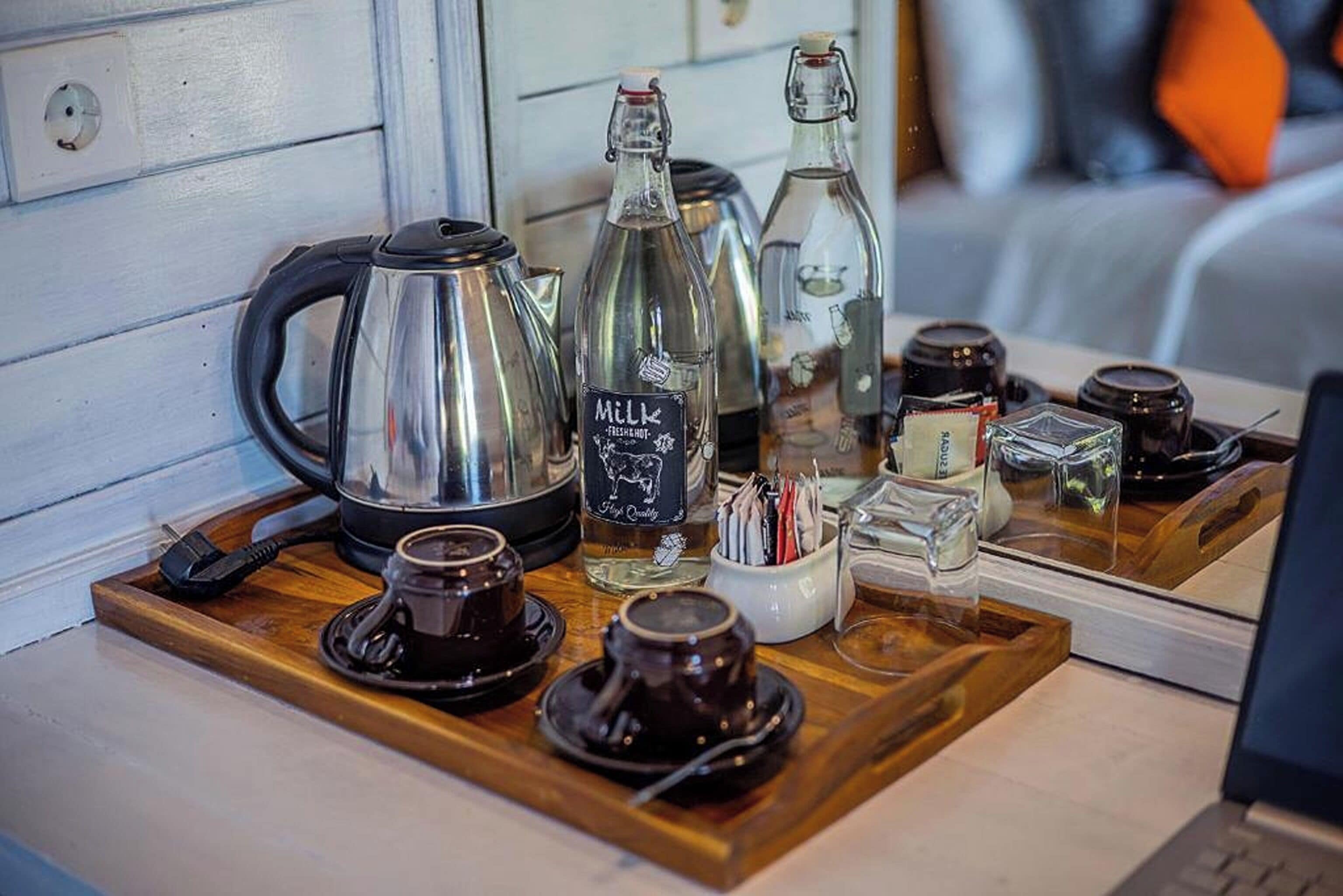 A wooden tray with a coffee maker, a milk bottle, and various cups and mugs.