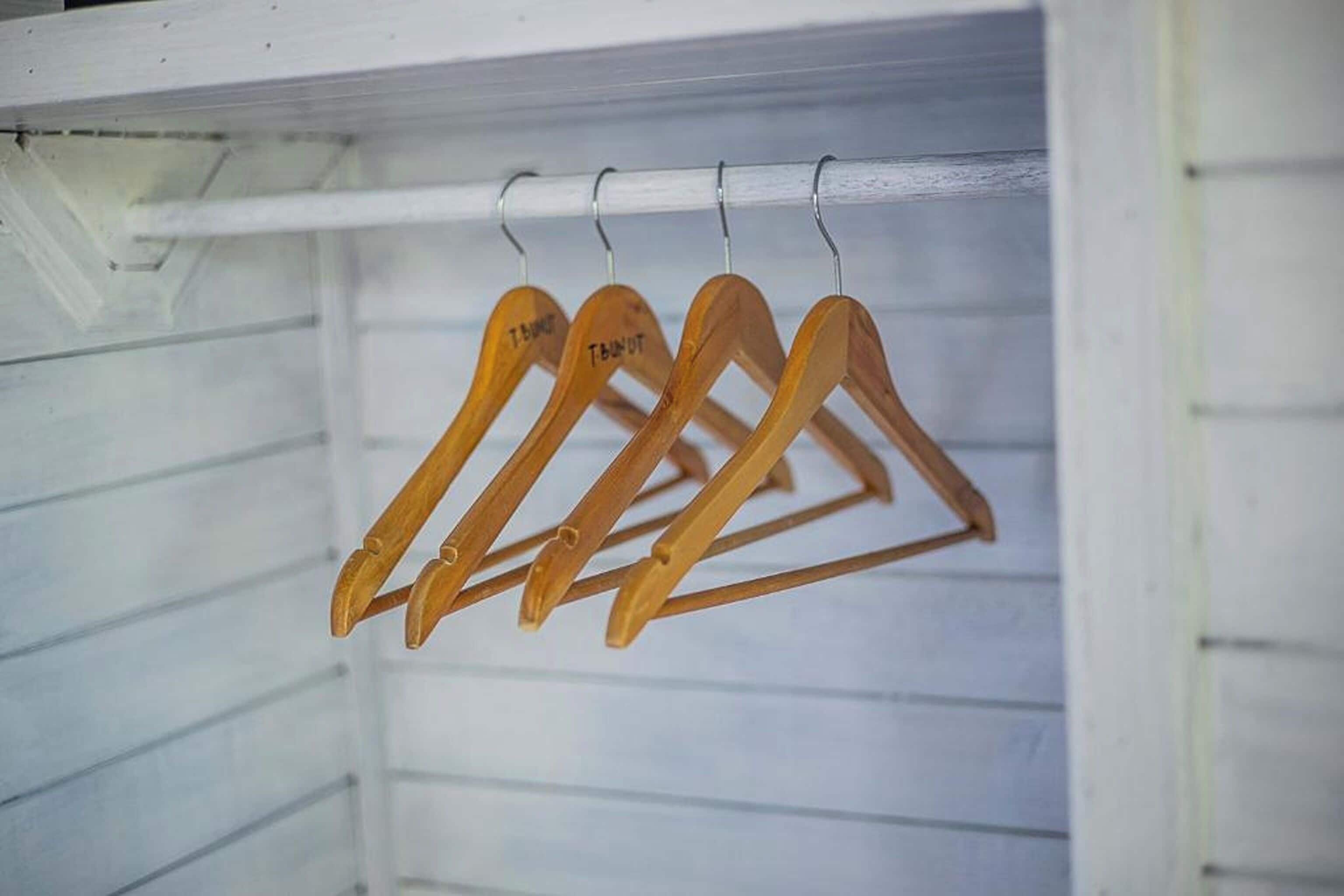 A wooden hanger rack with hangers labeled 'TNT' in a white room.