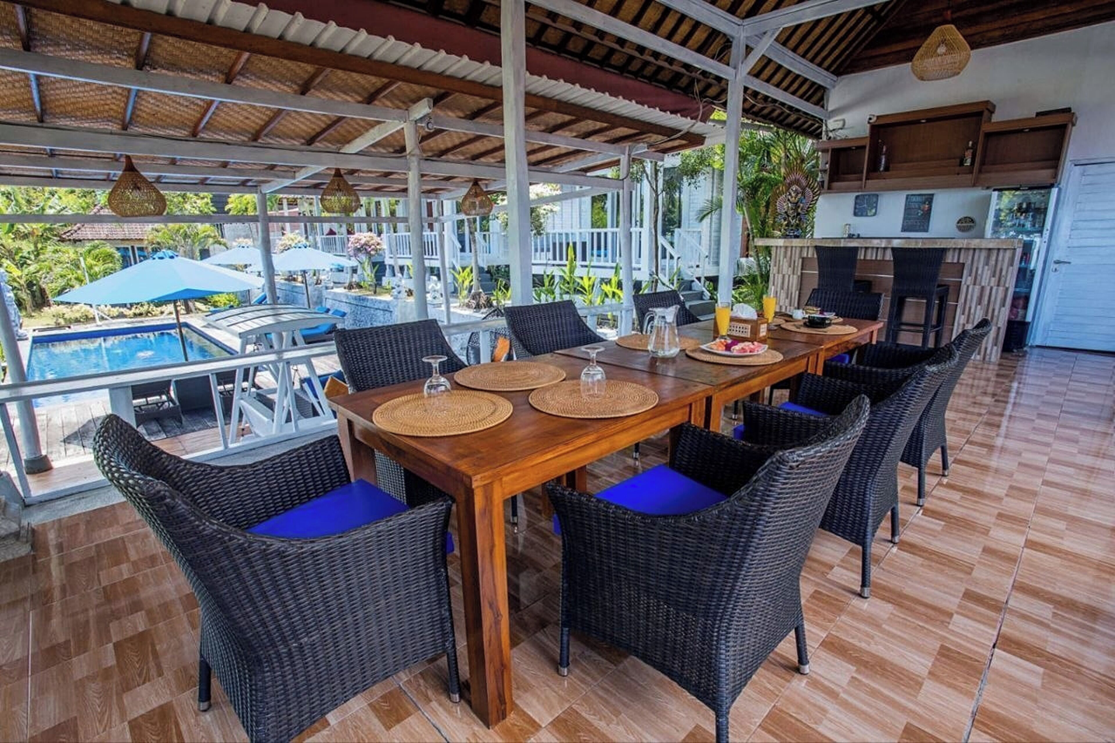Un espace de restauration en plein air, avec des chaises en osier et une table en bois, offrant une vue sur une piscine et une végétation luxuriante.