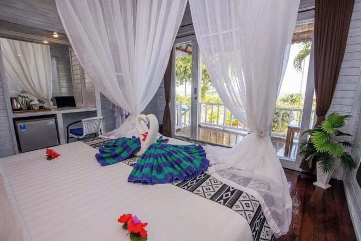 A bedroom with a bed, a desk, and a view of the outdoors.
