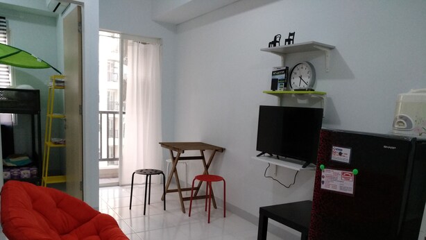A compact living space with a red chair, a small table, a TV, and a refrigerator. - RJB at Ayodhya Tangerang (Tangerang)