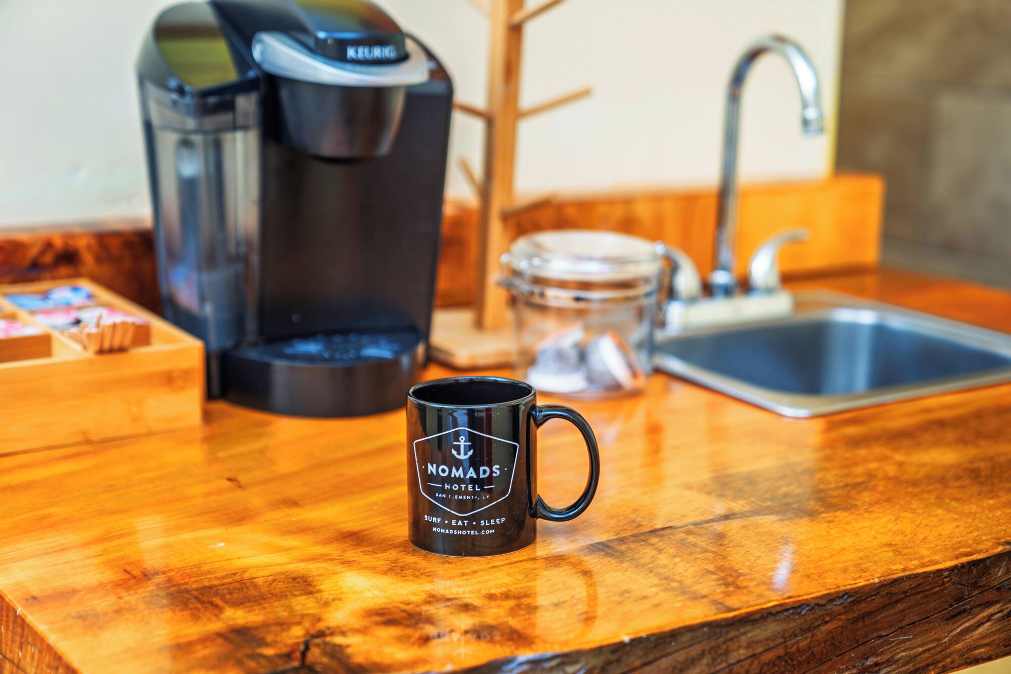 Eine Küchenarbeitsfläche mit Kaffeemaschine, Tasse, Glasbehälter und Spüle.