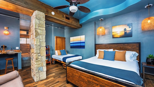 A modern hotel room with a large bed, a smaller bed, a desk, and a stone pillar. - Nomads Hotel - Near San Clemente Pier (San Clemente)