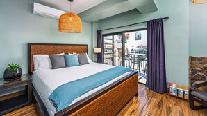 A bedroom with a wooden bed, a hanging light fixture, a potted plant, and a view of the outside balcony. - Nomads Hotel - Near San Clemente Pier (San Clemente)