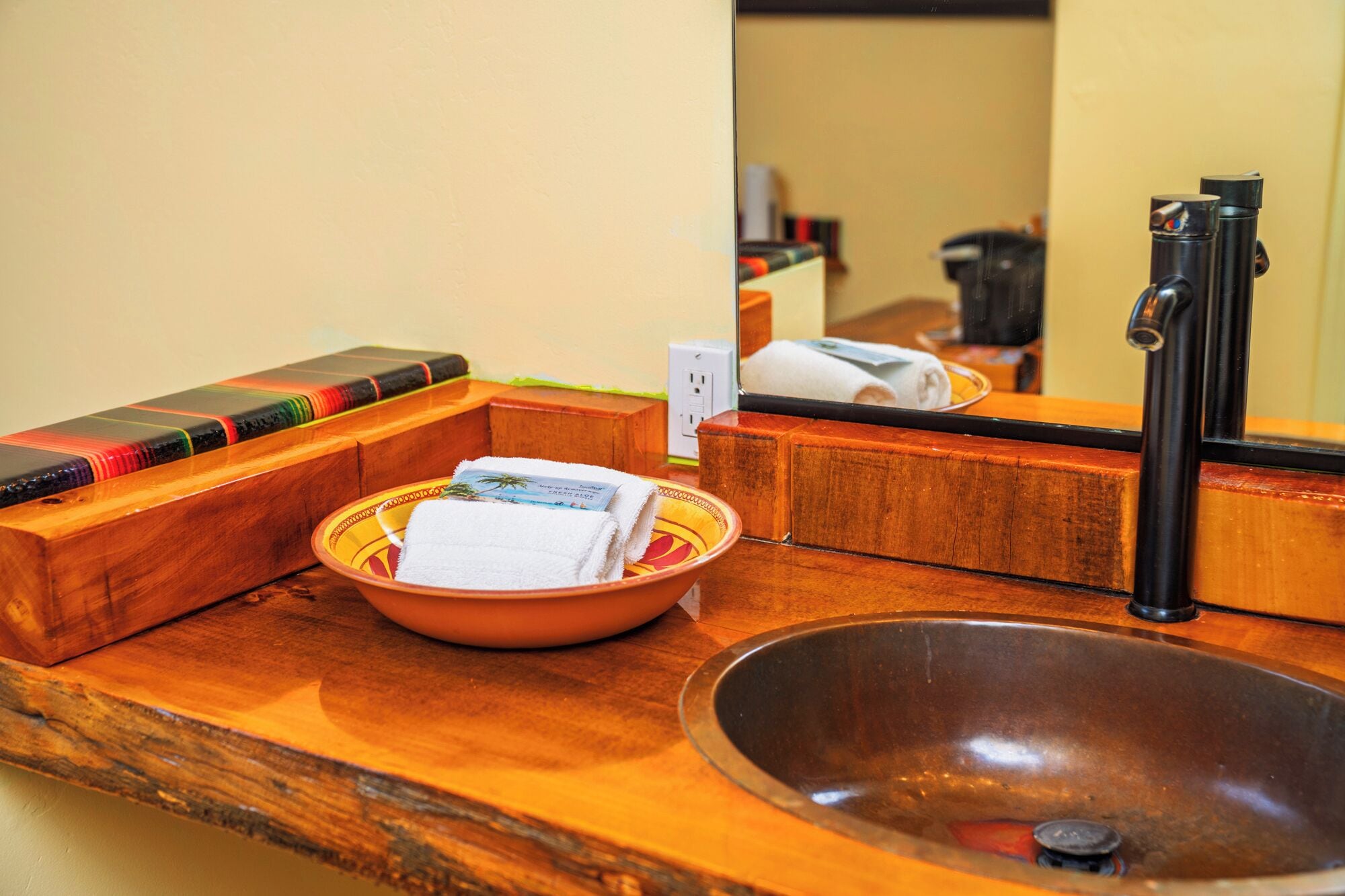 A wooden vanity with a sink, a bowl of toiletries, and a mirror.