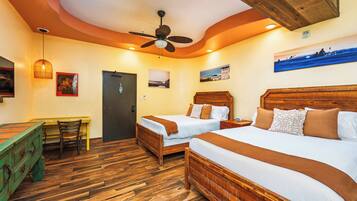 Quarto de hotel com duas camas, piso de madeira, ventilador de teto e obras de arte nas paredes.