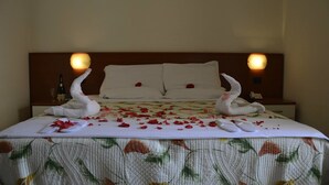 Un letto rifatto con cura, decorato con petali di rosa e asciugamani a forma di cigno, una bottiglia e un bicchiere sul comodino.