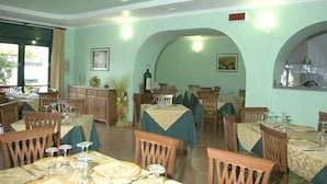 Zona pranzo con diversi tavoli e sedie, angolo cottura e un'ampia porta ad arco.