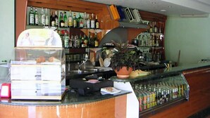 Un'area bar con un bancone, scaffali pieni di bottiglie di liquori, una pianta in vaso e una vetrina.