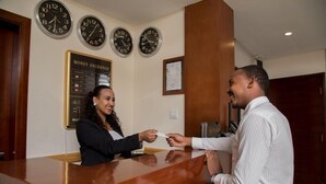 Un mostrador de recepción con relojes y un cartel de cambio de divisas al fondo.