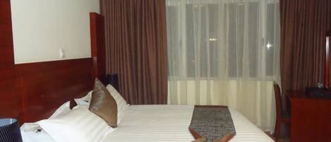 A hotel room with a large bed, a desk, and a window with curtains.