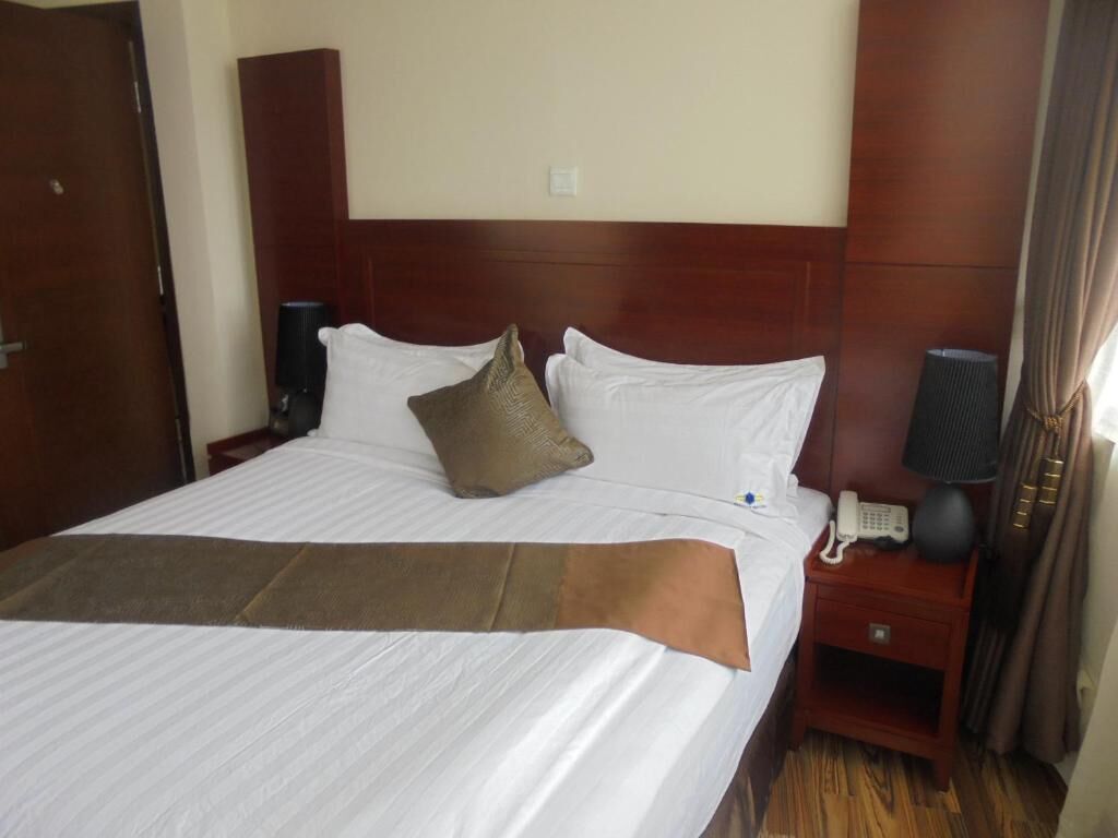 Habitación de hotel con una cama grande, cabecera de madera, mesita de noche con lámpara y teléfono.