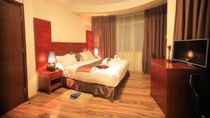 Una habitación de hotel con una cama grande, televisor, piso de madera y un escritorio con lámpara.