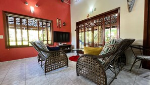 Ein Wohnzimmer mit Rattanmöbeln, einem Fernseher und einem großen Fenster mit dekorativen Gitterstäben.