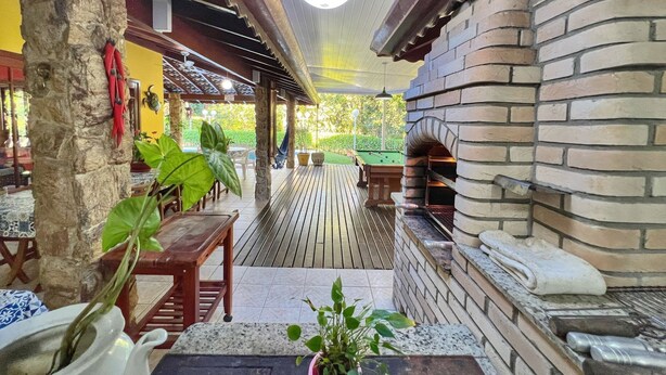 Eine Terrasse im Freien mit einem Backofen aus Ziegelsteinen, Holztischen und Kübelpflanzen.