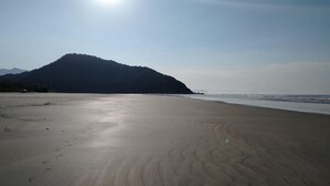Ein Strand mit einem Berg im Hintergrund und Fußabdrücken im Sand.
