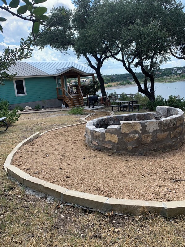 A lakeside cabin with a stone fire pit, outdoor seating, and a covered porch.