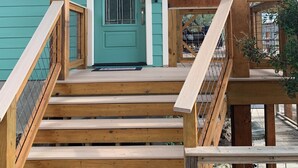Una escalera de madera que conduce a una puerta turquesa con diseño de estrella, rodeada de vigas y barandales de madera.