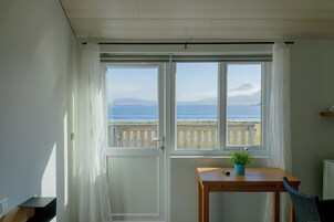 Una habitación con vistas al mar y a la montaña, una mesa de madera con una planta, y una silla.