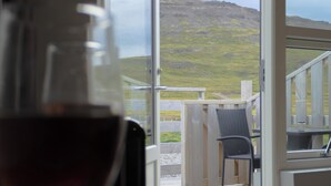 Een glas rode wijn op een tafel, met uitzicht op een houten terras en een grasheuvel op de achtergrond.
