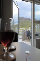 Una copa de vino tinto sobre una mesa, con vista a una terraza de madera y una colina cubierta de hierba al fondo.
