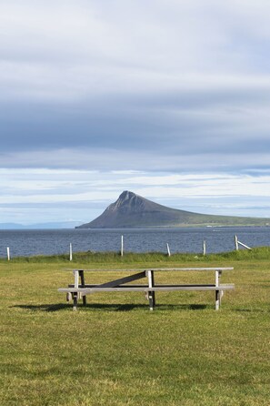 A grassy area with a picnic table and a view of a mountain across a body of water. - Urðartindur Guesthouse (Nordurfjordur)