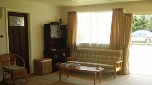Una sala de estar con un sofá, una mesa de centro de madera, un mueble para televisor y una silla de mimbre.