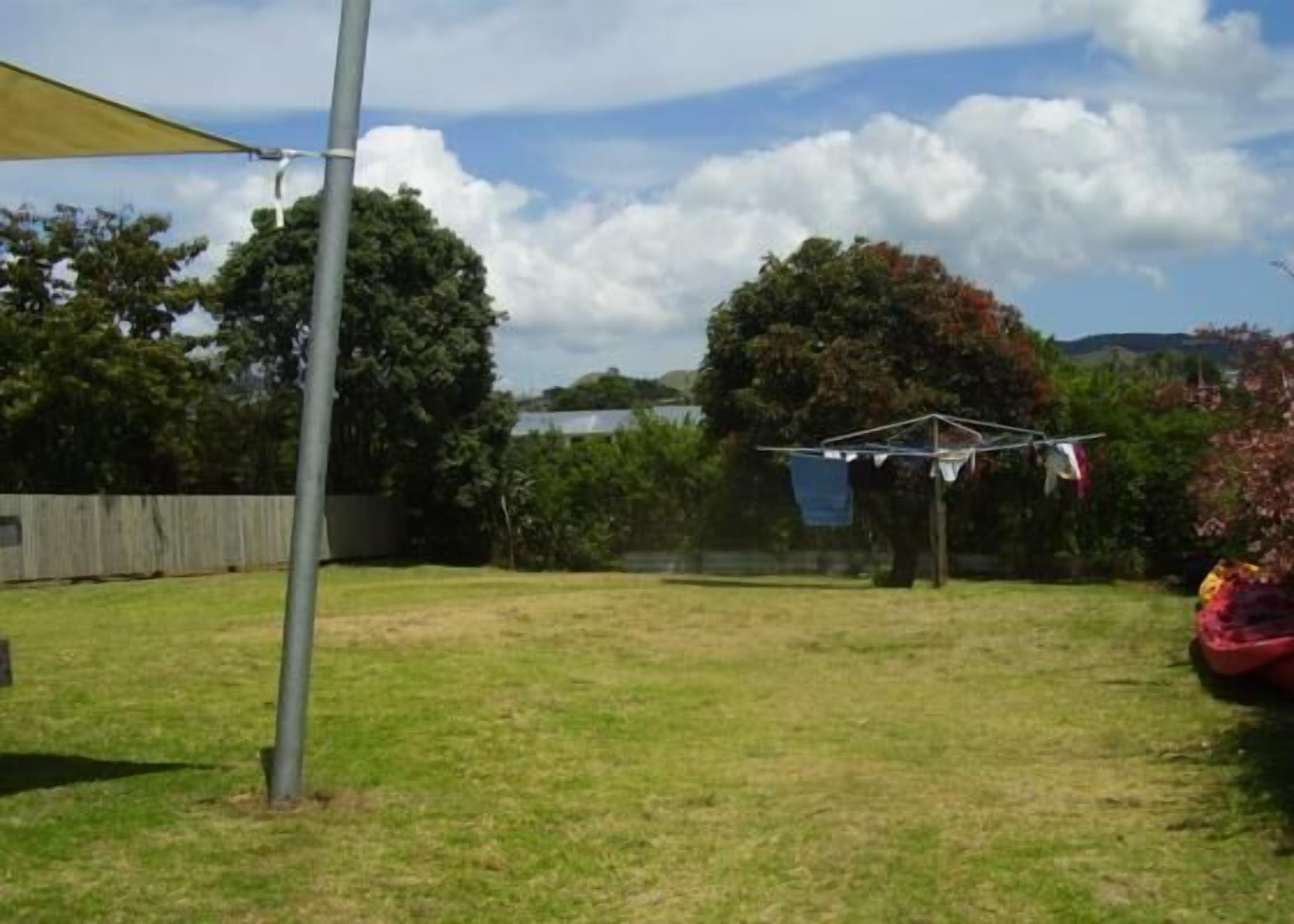 A grassy backyard with a clothesline, a wooden fence, and trees.