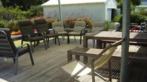 Un patio exterior con suelo de madera, una mesa y varias sillas.