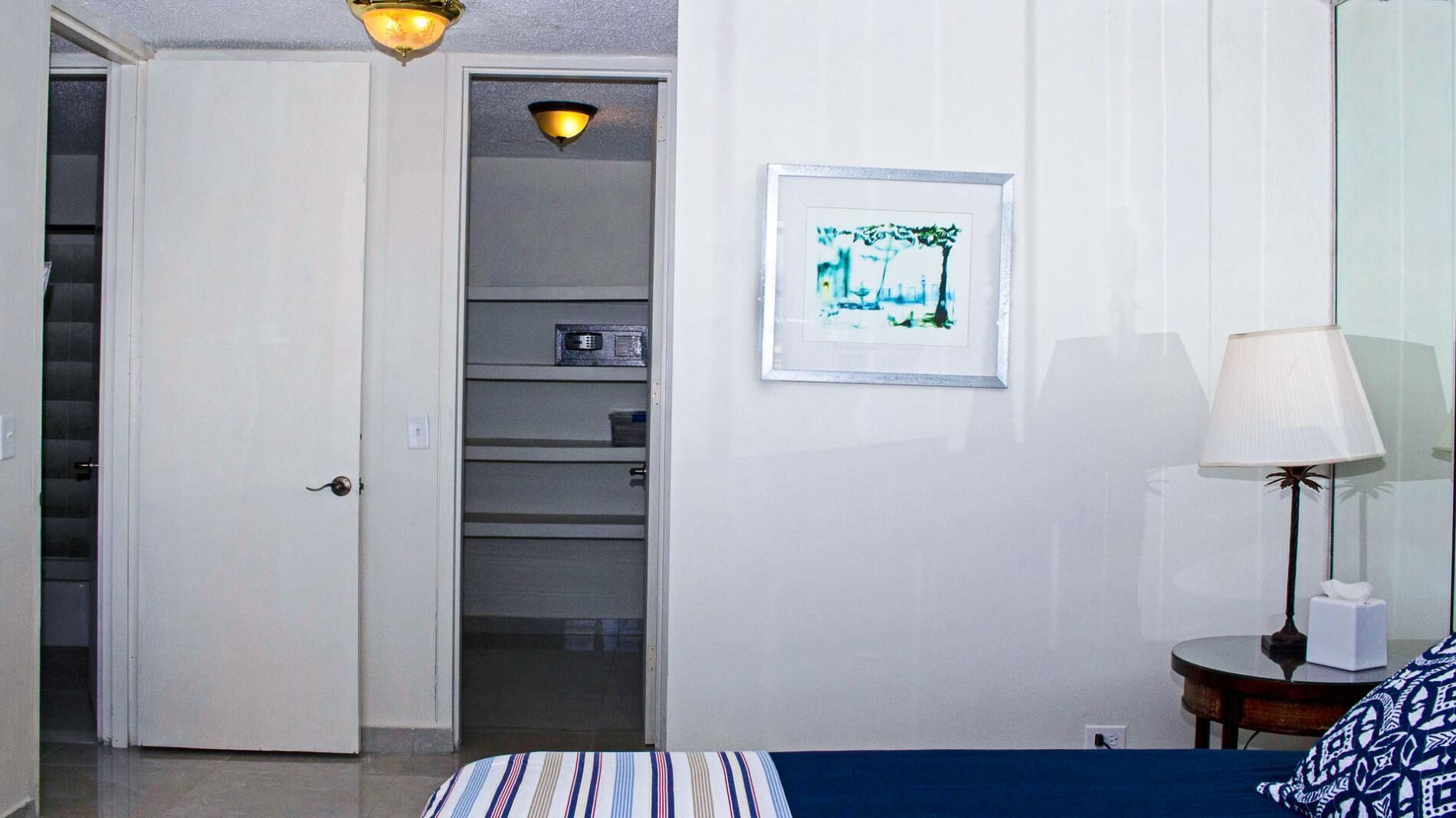 A hotel room with a bed, a bedside table with a lamp, a framed picture on the wall, and a closet with shelves.