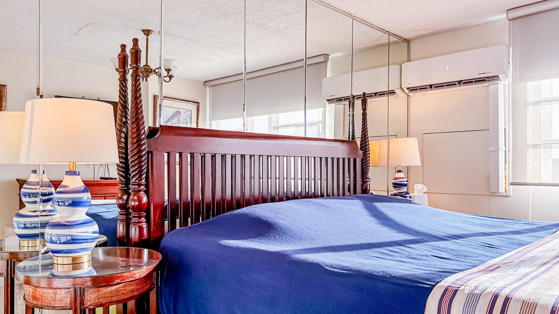 A hotel room with a large bed, a wooden headboard, two bedside tables with lamps, and a large window with an air conditioning unit.