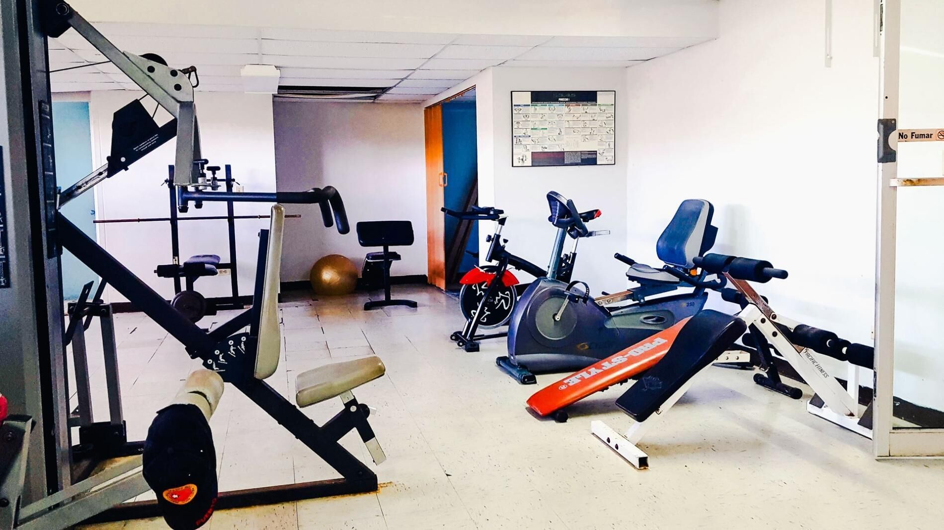 Un gimnasio con equipo de ejercicio diverso, incluyendo una cinta de correr, bicicleta estática y máquinas de pesas.