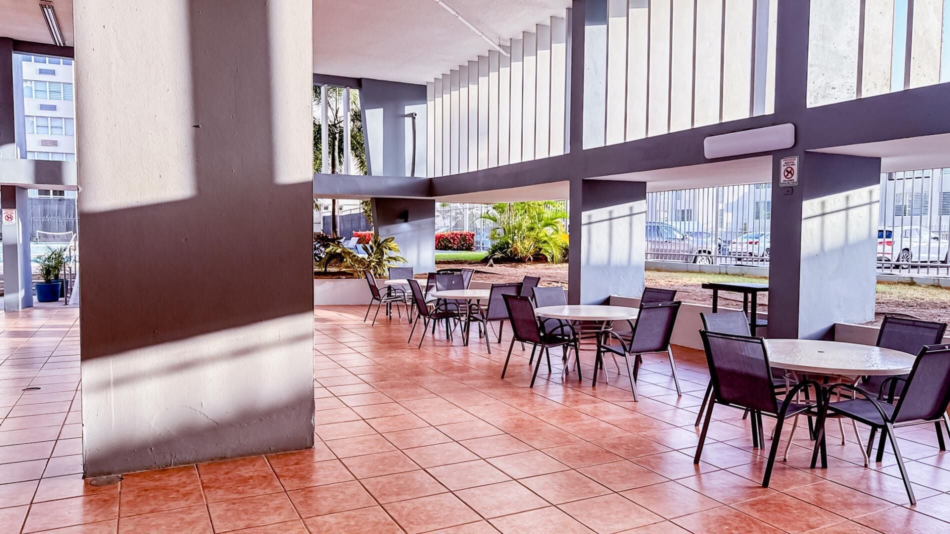 Un vaste espace extérieur aménagé pour les repas, avec de nombreuses tables et chaises, de grandes fenêtres et une vue sur le paysage urbain.