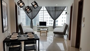 A modern living room with a dining area, large windows with curtains, a flat-screen TV, and a city view. - SUPER VALUE APARTMENT near KLCC Twin Tower/ KL City Centre (Kuala Lumpur)