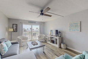 Ein Wohnzimmer mit Deckenventilator, Fernseher und einem Schild mit der Aufschrift 'BEACH HOUSE'.