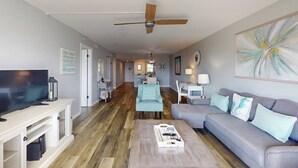 A modern living room with a television, sofa, and coffee table. A hallway leads to a dining area with a table and chairs.