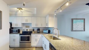 A modern kitchen with white cabinets, stainless steel appliances, granite countertops, and a built-in dishwasher.