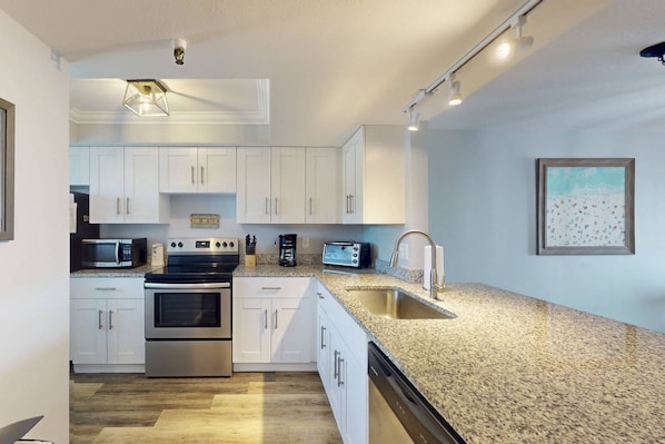 A modern kitchen with white cabinets, stainless steel appliances, granite countertops, and a built-in dishwasher.
