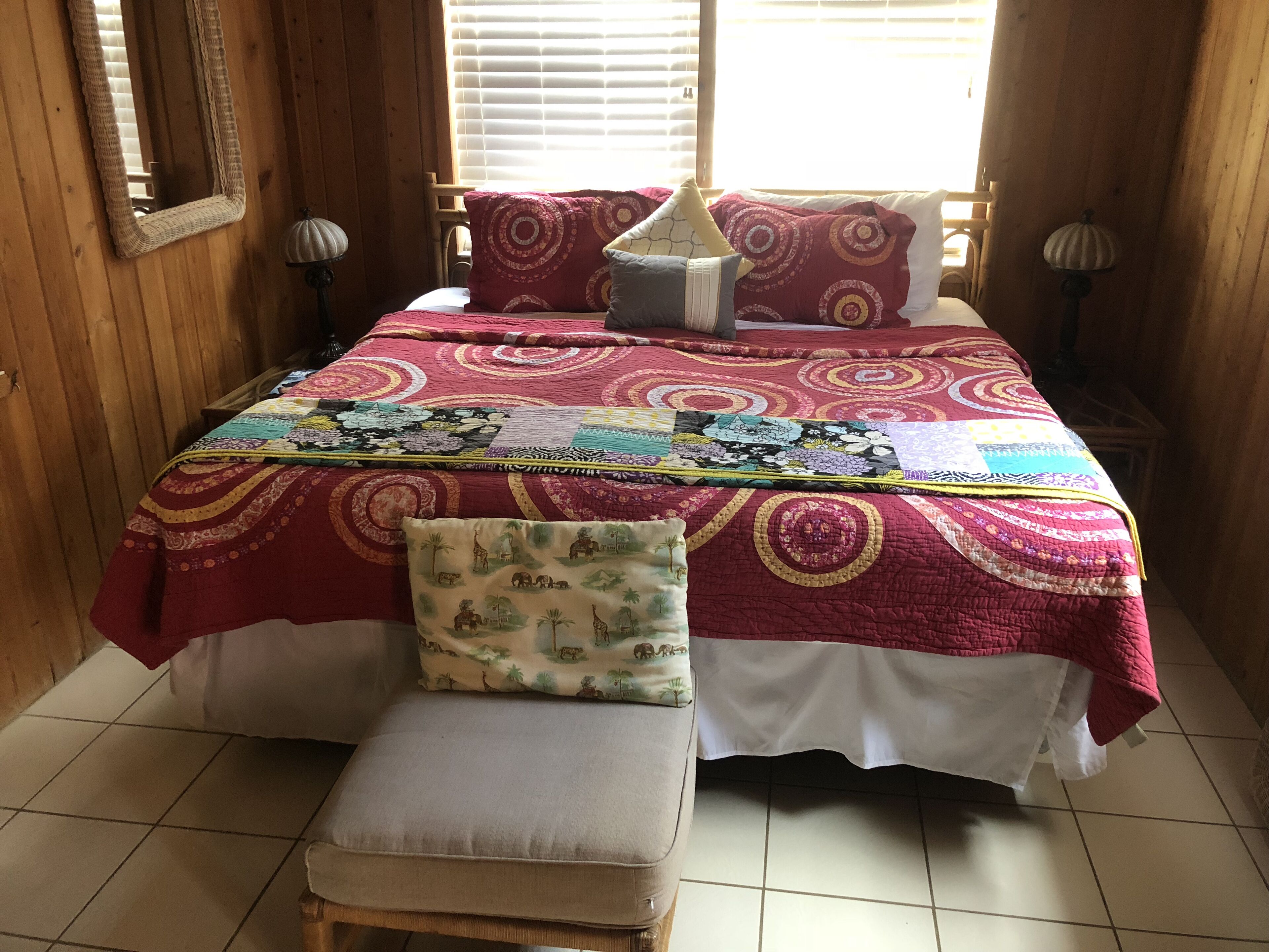 Un lit recouvert d’une couvre-lit à motifs rouges et blancs, d’une courtepointe et d’un oreiller à imprimés d’animaux. Devant le lit, on trouve un banc avec un coussin.