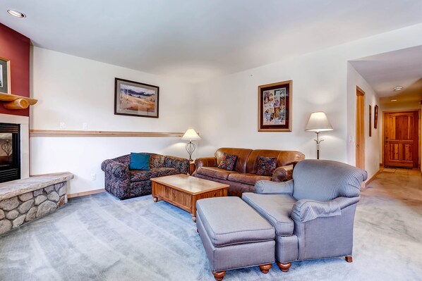Una sala de estar con chimenea de piedra, un sofá de cuero marrón, un sillón estampado y una mesa de centro de madera.