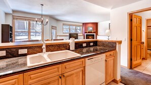 A modern kitchen with granite countertops, wooden cabinets, a built-in dishwasher, and a large window providing natural light.