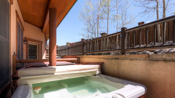 A hot tub with a wooden deck, stone wall, and a view of trees.
