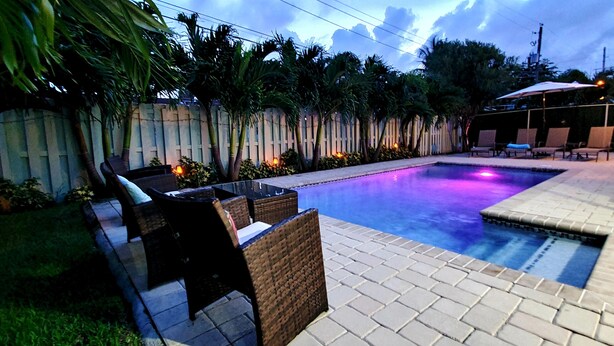 A swimming pool with lounge chairs and a small hot tub area, surrounded by a wooden fence and palm trees. - SUNSHINE DREAM HOUSE WITH HEATED POOL, NEAR BEACH, CLOSE TO SOUTH BEACH (Dania Beach)