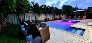 A swimming pool with lounge chairs and a small hot tub area, surrounded by a wooden fence and palm trees. - SUNSHINE DREAM HOUSE WITH HEATED POOL, NEAR BEACH, CLOSE TO SOUTH BEACH (Dania Beach)