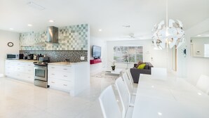 A modern kitchen with a checkered backsplash, stainless steel appliances, and a dining area with white chairs and a table. - SUNSHINE DREAM HOUSE WITH HEATED POOL, NEAR BEACH, CLOSE TO SOUTH BEACH (Dania Beach)