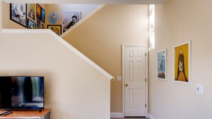 A hallway with a staircase, a flat-screen TV on a wooden stand, and various framed artworks on the walls. - 4BR Regal Palms Townhome by FS FL VH-154 (Davenport)