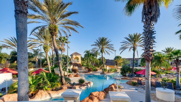 A resort pool area with palm trees, a central pool, and a building in the background. - 4BR Regal Palms Townhome by FS FL VH-154 (Davenport)